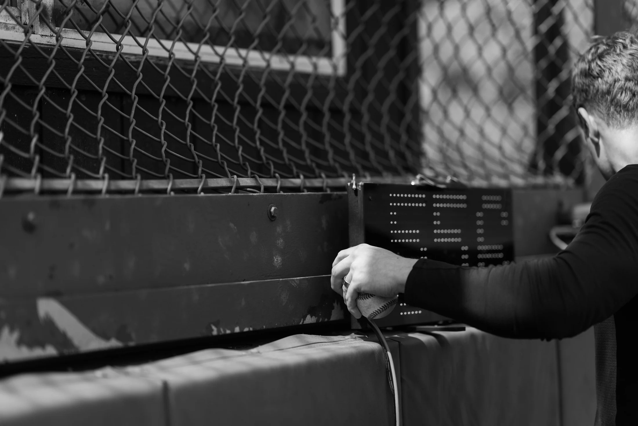 Rubicon coach holding a baseball beside a fence and radar display